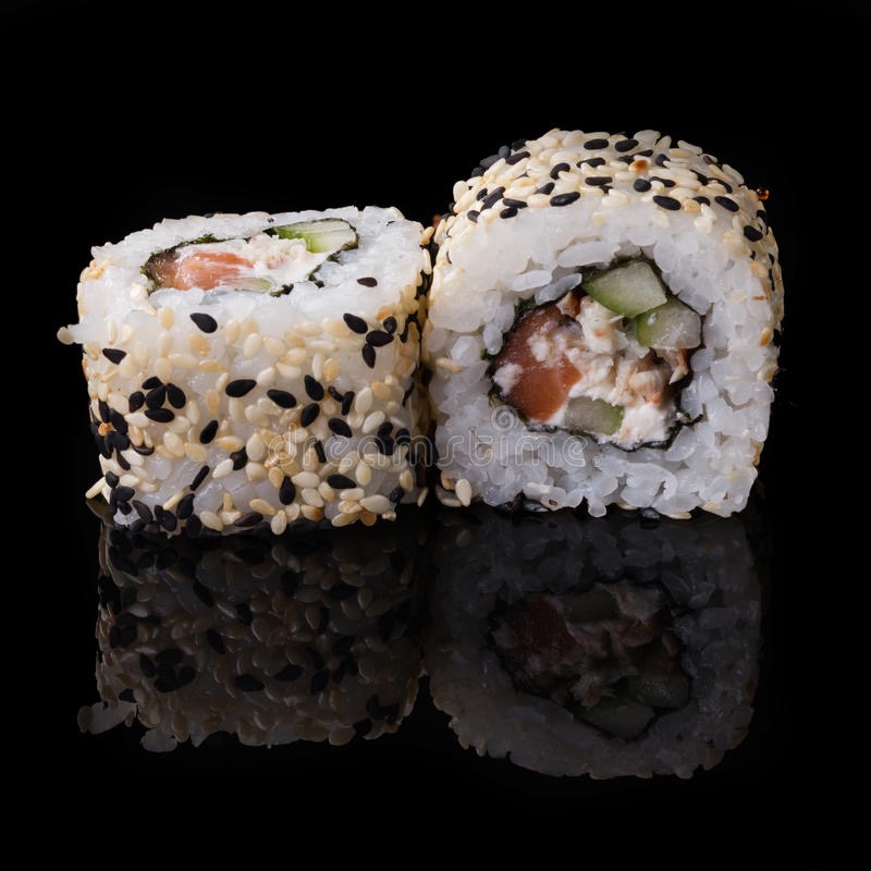 Dwa kawałki sushi z łososiem, ogórkiem i białym serkiem, posypane białym i czarnym sezamem, leżące na czarnym, błyszczącym tle.