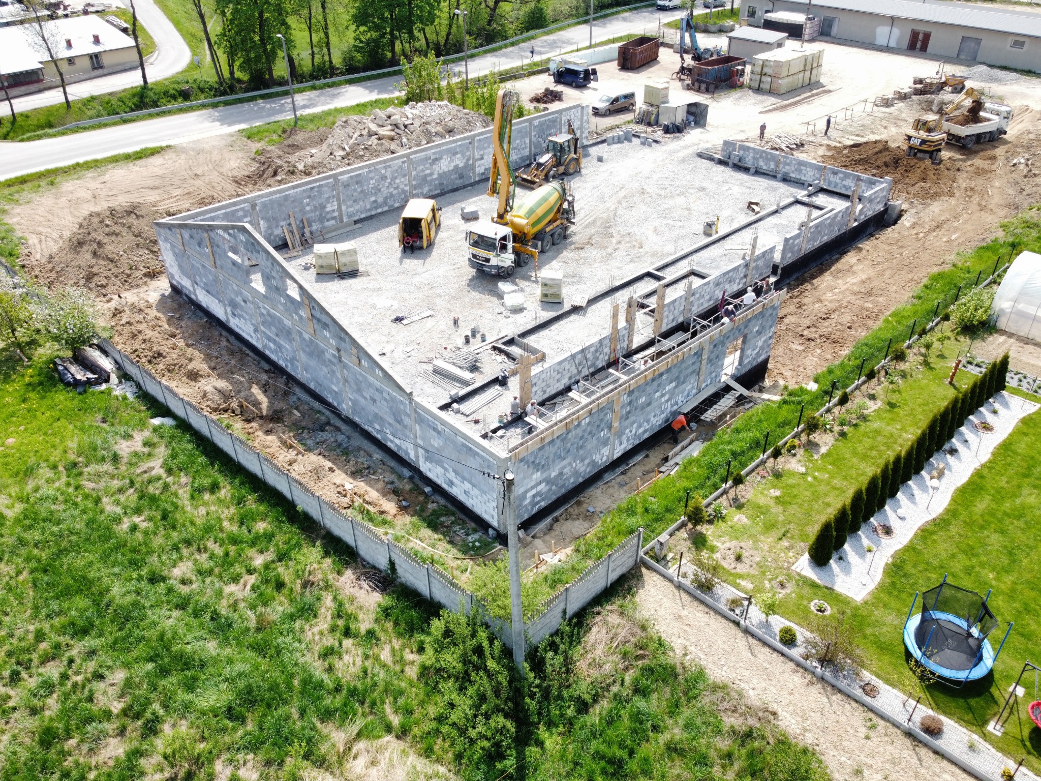 Budowa domu z bloczków betonowych, widok z góry, z betoniarką i pompą do betonu na placu budowy, teren częściowo uporządkowany, w tle widoczny skład budowlany.