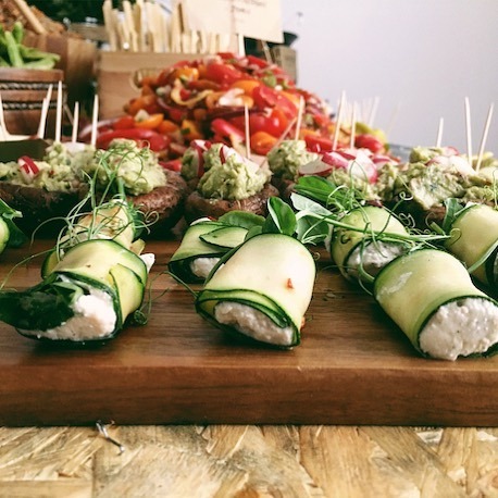 Elegancko podane przekąski: roladki z cukinii z kremowym nadzieniem, grzyby z guacamole, kolorowa sałatka warzywna na drewnianej desce.