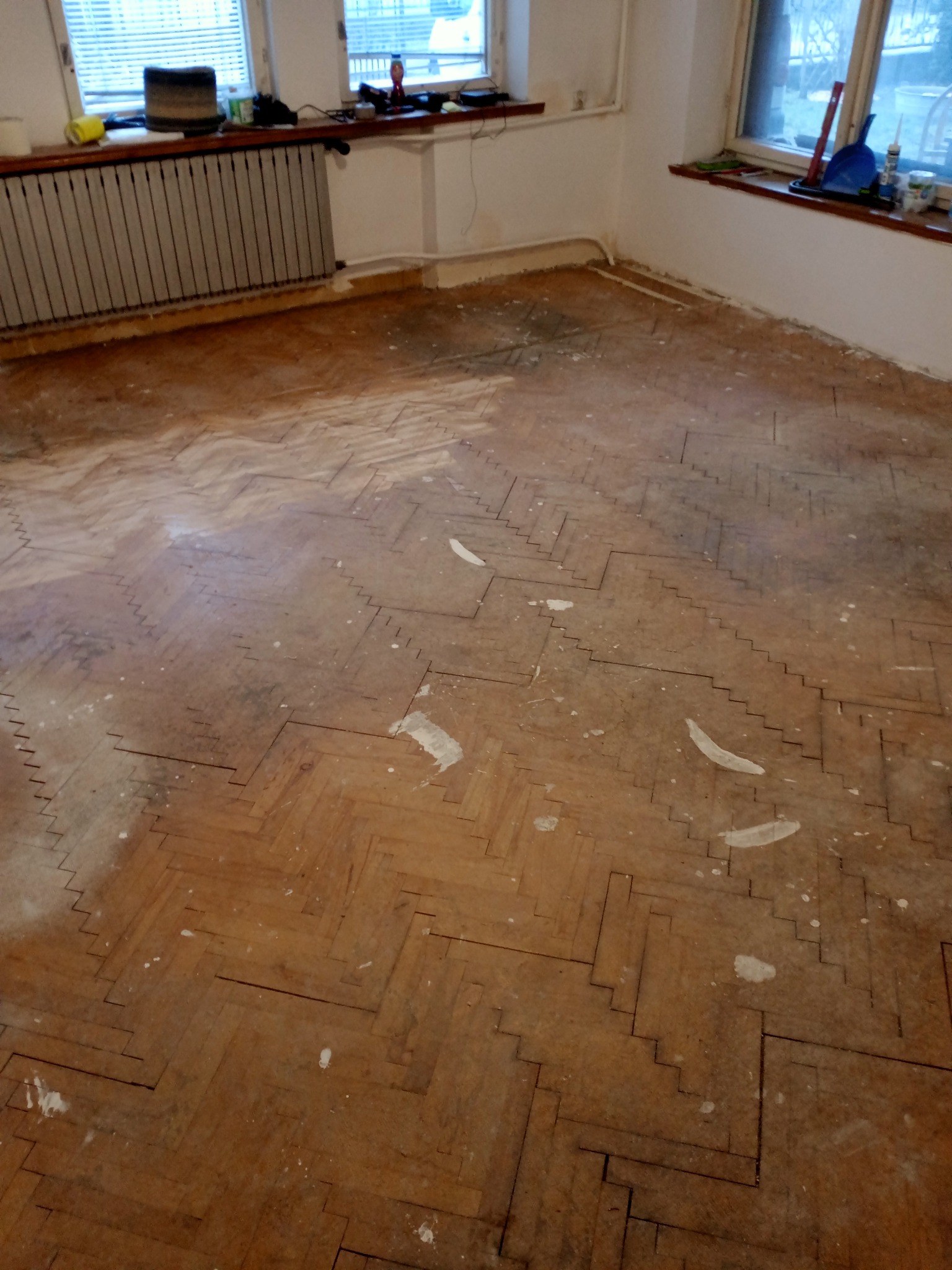 Parkiet ułożony w jodełkę przed cyklinowaniem, widoczne ślady po farbie i starej warstwie lakieru, przygotowany do renowacji.