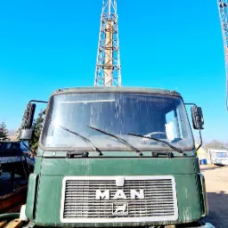 Zielony, brudny samochód ciężarowy MAN na tle wieży wiertniczej i błękitnego nieba, z widoczną tablicą rejestracyjną FMI 44817.