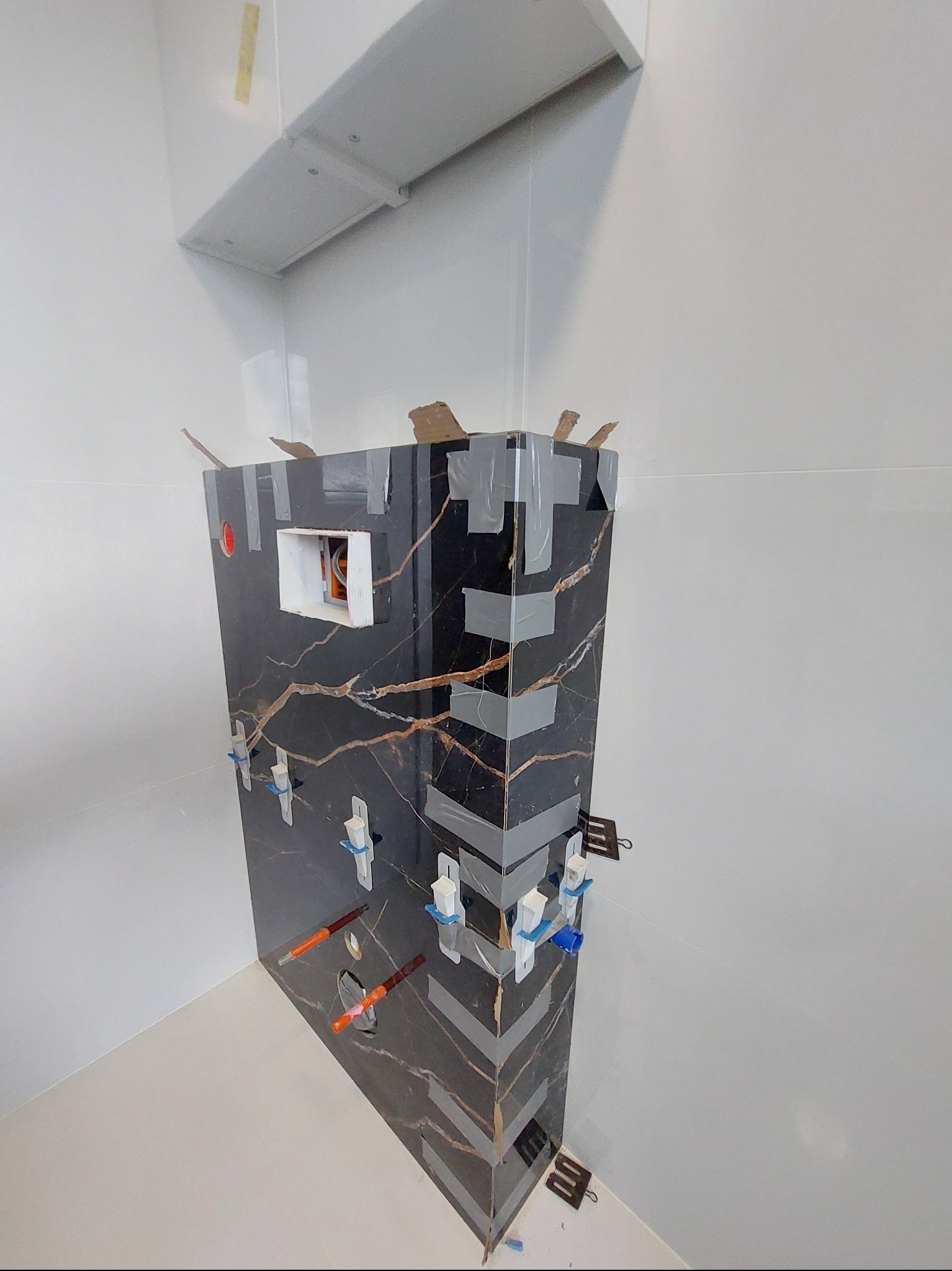 Montaż stelaża podtynkowego WC obłożonego płytkami imitującymi marmur, zabezpieczonego taśmą i klinami poziomującymi, w trakcie prac wykończeniowych łazienki.