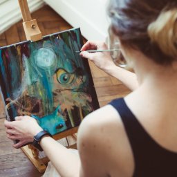 Sylwia Kos Fotografia - Artystka w Markach maluje na płótnie fantazyjny obraz z motywem oka i kota, używając cienkiego pędzla i farb akrylowych.