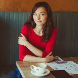 Sylwia Kos Fotografia - Portret kobiety w czerwonej bluzce siedzącej przy stole w kawiarni, z filiżanką po kawie i rozłożonymi materiałami edukacyjnymi.