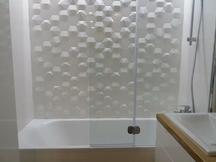 Biała łazienka w Warszawie z wanną, szklanym parawanem i ścianą wyłożoną trójwymiarowymi płytkami w kształcie heksagonów.