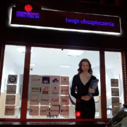 Fasada budynku agencji ubezpieczeniowej z podświetlanym szyldem 'DOM UBEZPIECZENIOWY SPECTRUM' i napisem 'twoje ubezpieczenia', w oknie naklejki z logotypami różnych towarzystw ubezpieczeniowych...