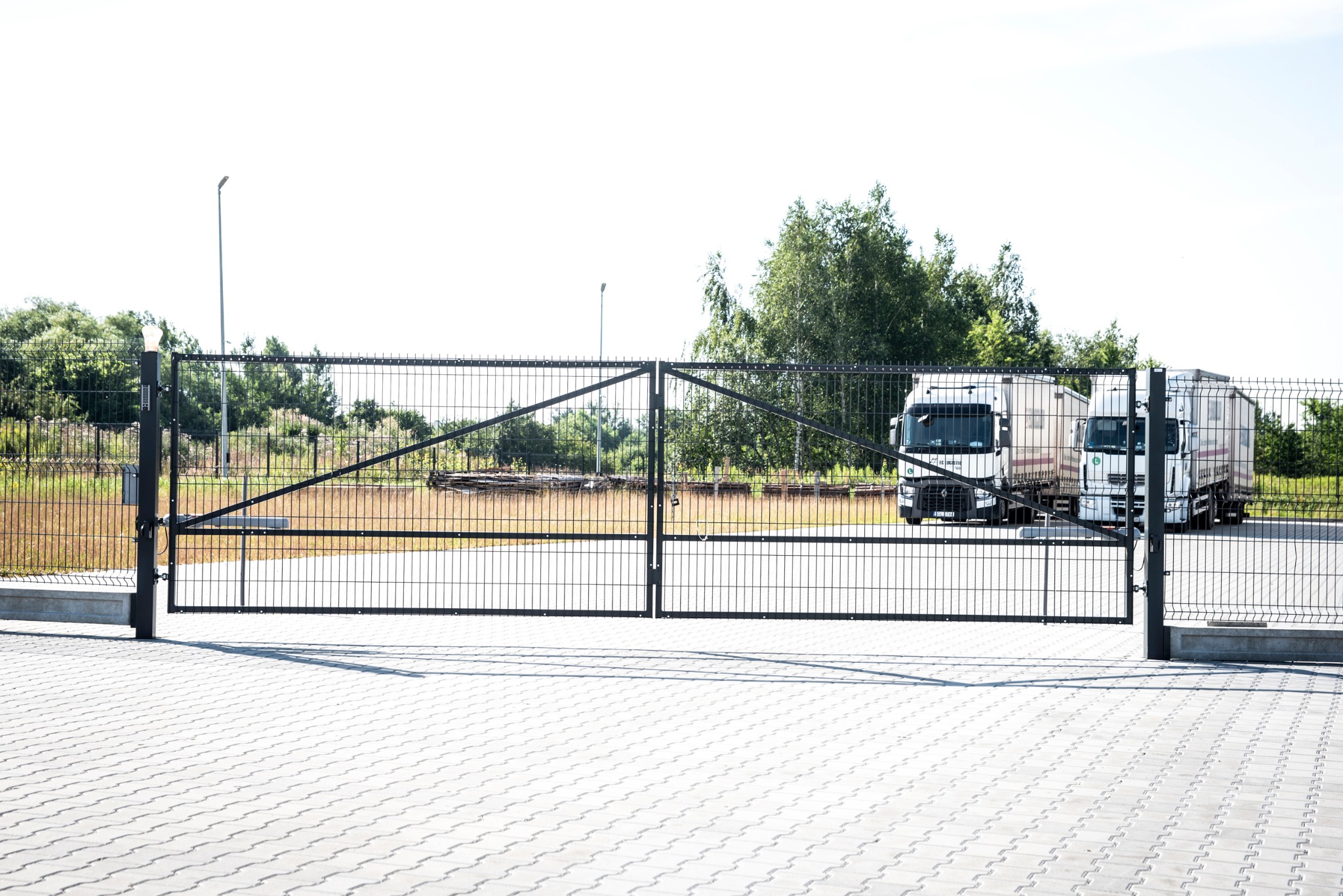 Otwarta, dwuskrzydłowa brama z paneli metalowych w Pyskowicach, z widocznymi dwoma samochodami ciężarowymi w tle.