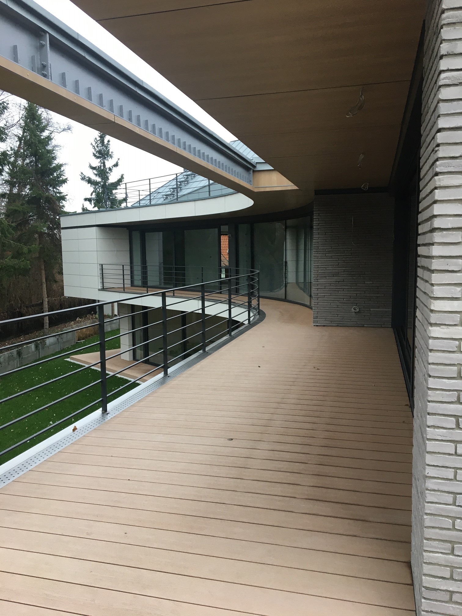 Nowoczesny dom z drewnianym tarasem, balustradą i nietypową konstrukcją dachu.