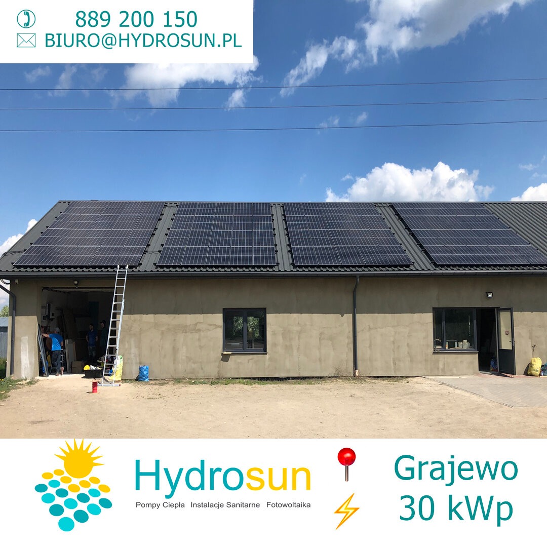 Instalacja paneli słonecznych na dachu budynku gospodarczego, widoczna drabina oparta o ścianę, ekipa montażowa w tle, logo firmy w dolnej części zdjęcia.