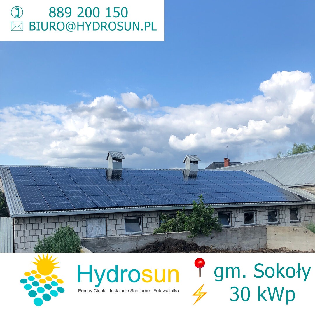 Instalacja paneli słonecznych na dachu budynku gospodarczego z cegły, widoczne dwa kominy wentylacyjne, błękitne niebo z chmurami w tle, w dolnej części zdjęcia logo firmy Hydrosun.
