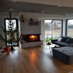 Nowoczesny salon z szarym narożnikiem, płonącym paleniskiem i choinką z prezentami, widok z perspektywy podłogi.