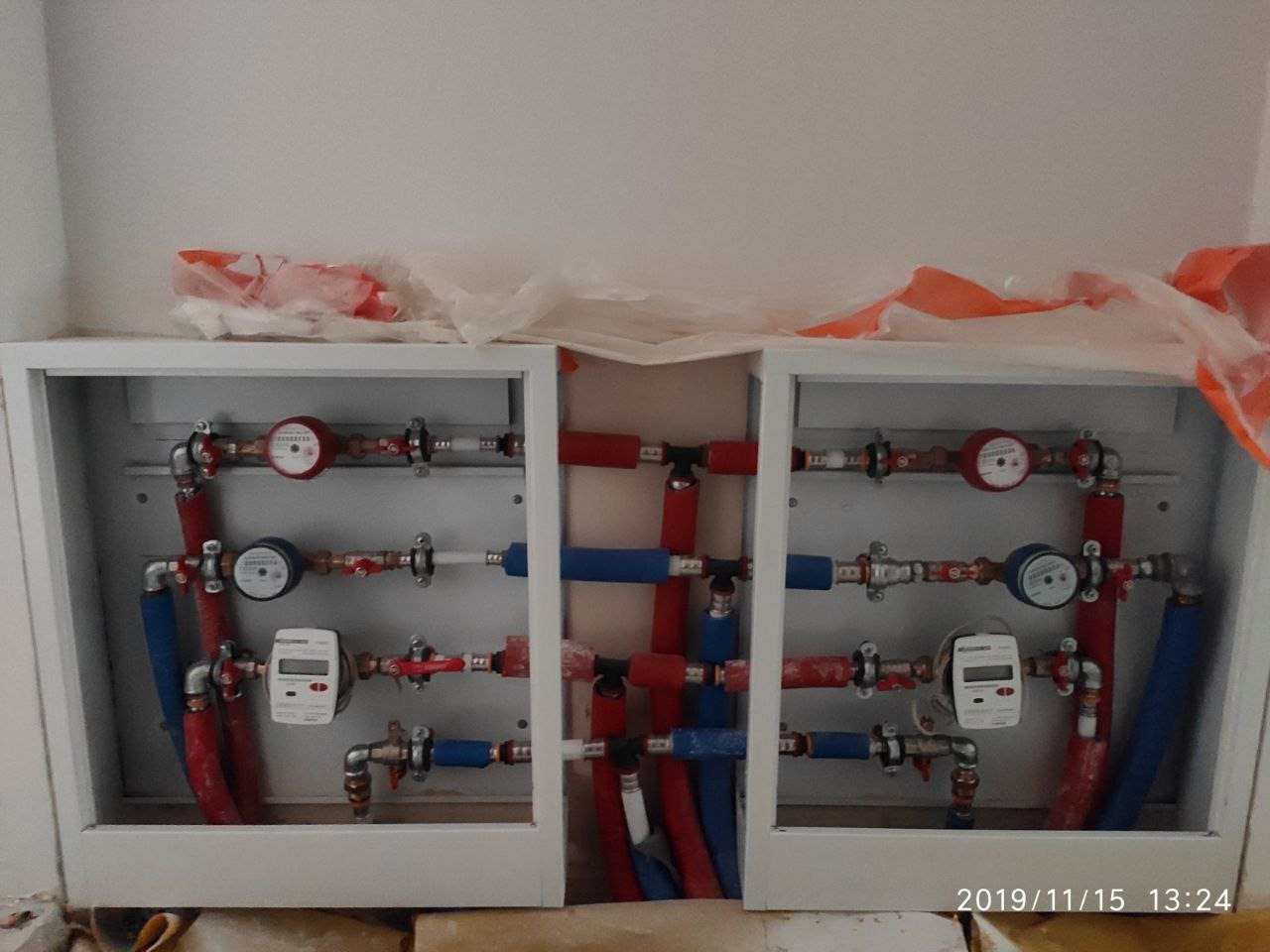 Rozdzielacz hydrauliczny w szafce, widoczne rury w kolorach czerwonym i niebieskim, liczniki wody z wyświetlaczami, instalacja połączona z rurami PEX.