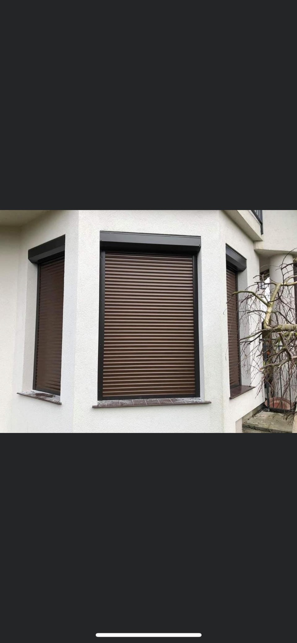 Brązowe osłony okienne zewnętrzne zamontowane w białej fasadzie budynku, widoczne trzy okna z zamkniętymi listwami.