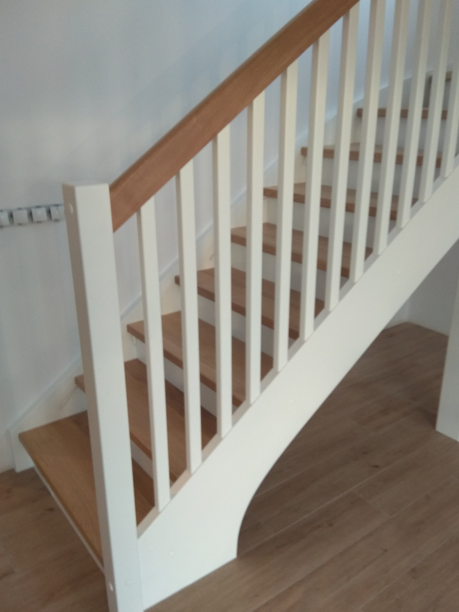 Drewniane schody z białymi balustradami i drewnianą poręczą, widok z dołu, jasne wnętrze.