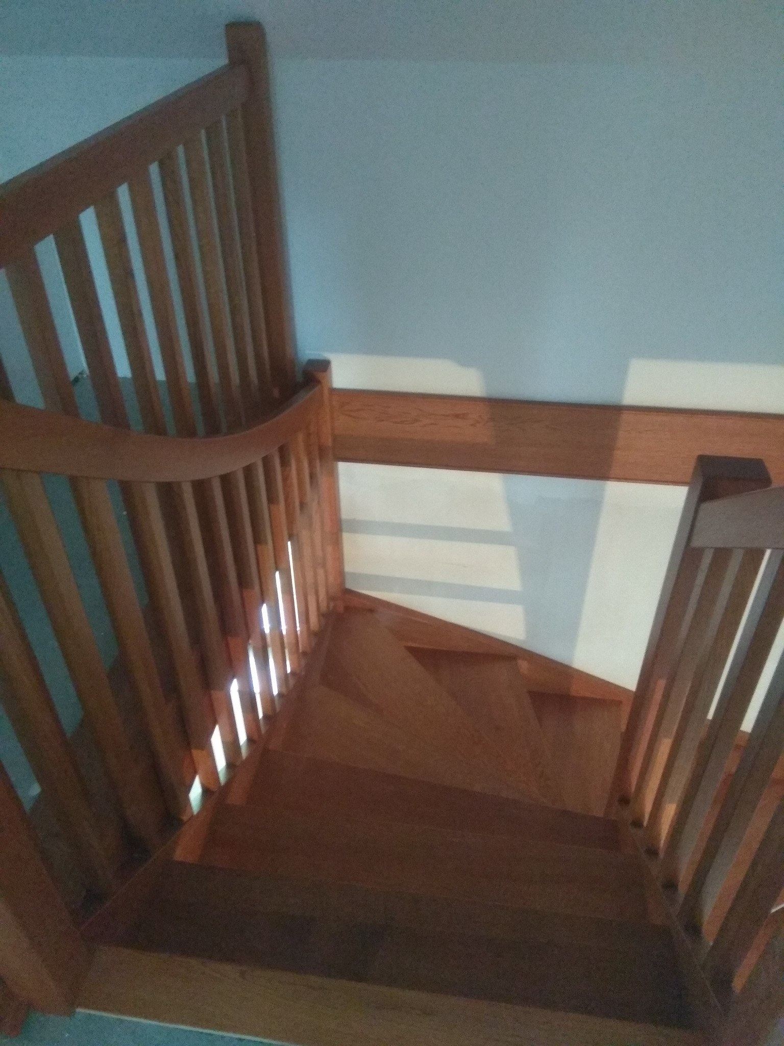 Kątowe ujęcie drewnianych schodów z balustradą, widoczne stopnie i pionowe elementy balustrady, oświetlone przez wpadające światło.