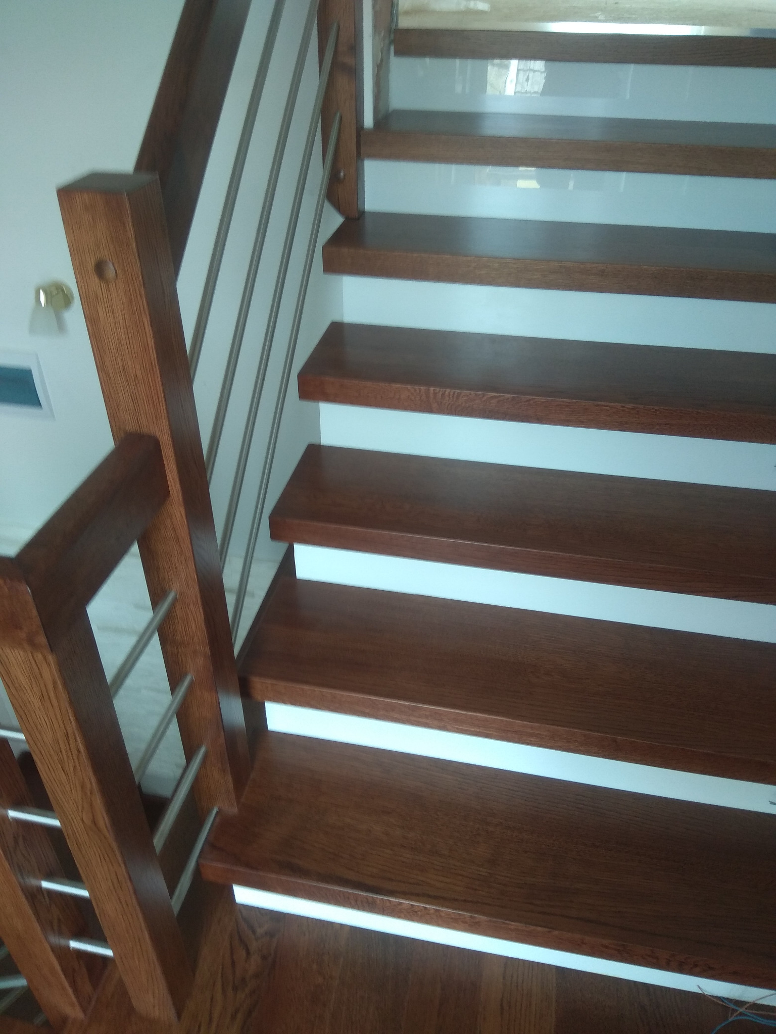 Nowoczesne schody z drewna o ciemnym odcieniu, z białymi podstopnicami i metalowymi balustradami, widok z dołu.