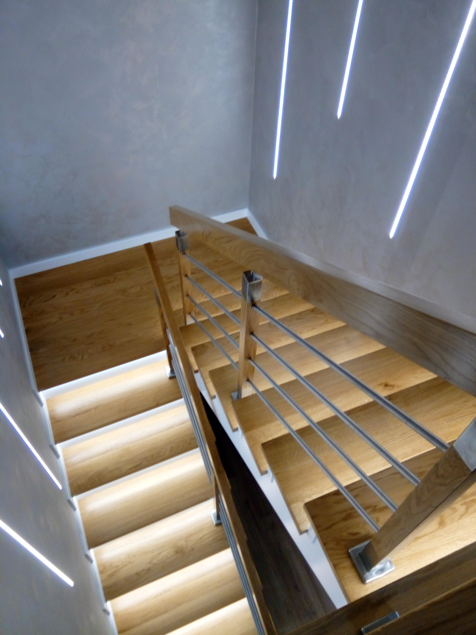 Nowoczesne schody z drewna z podświetleniem LED wzdłuż ściany i metalową balustradą, widok z góry.