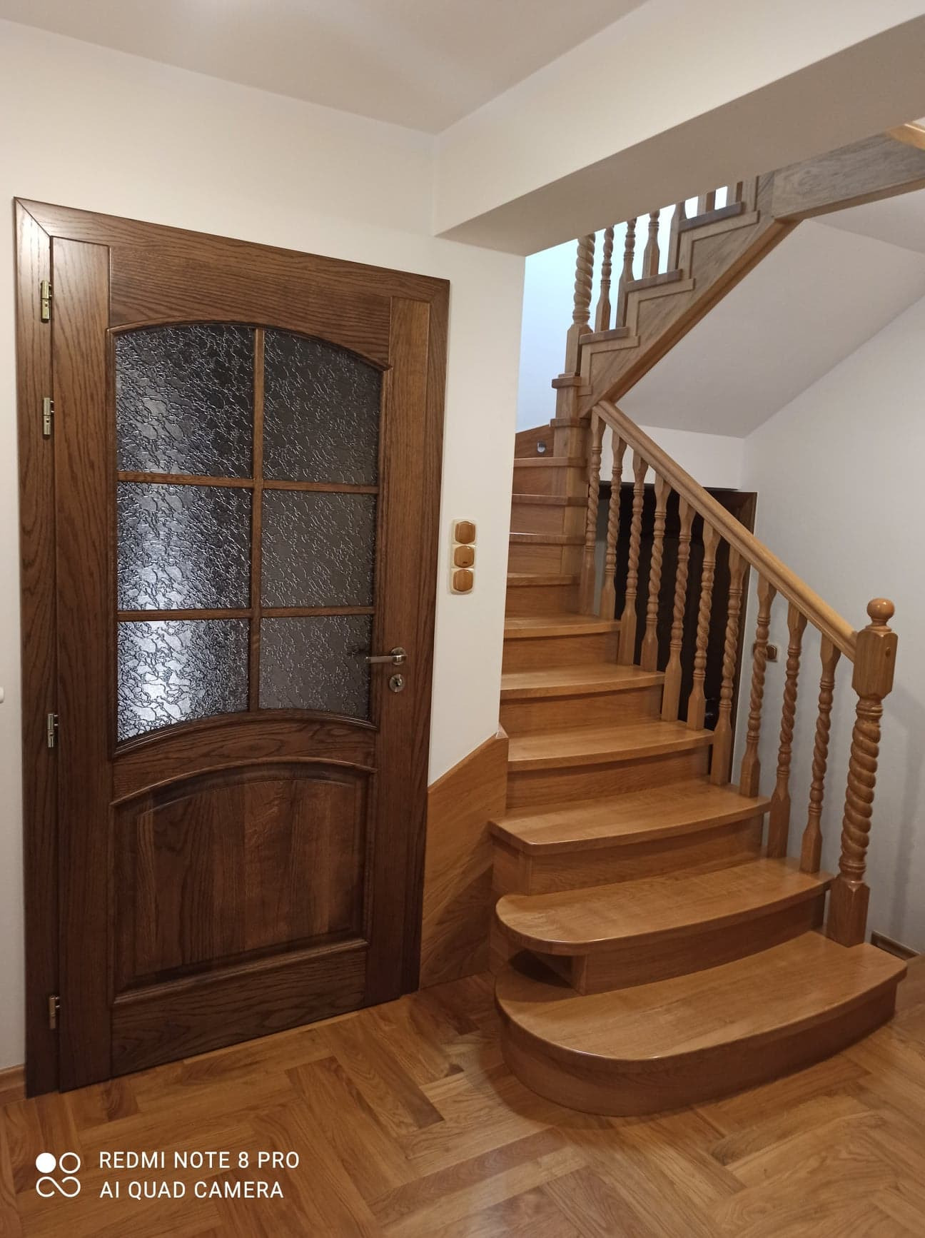 Drewniane schody z toczonymi balustradami i drewniana drzwi z szybą ornamentową, parkiet w jodełkę.