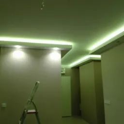 Wykończone wnętrze z podwieszanym sufitem z oświetleniem LED, widoczna drabina malarska, ściany w odcieniach beżu, oświetlenie punktowe.