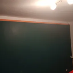 Świeżo pomalowana na ciemnozielono ściana z pomarańczową taśmą malarską przy suficie, widoczne akcesoria malarskie: puszka z farbą i niebieska taśma