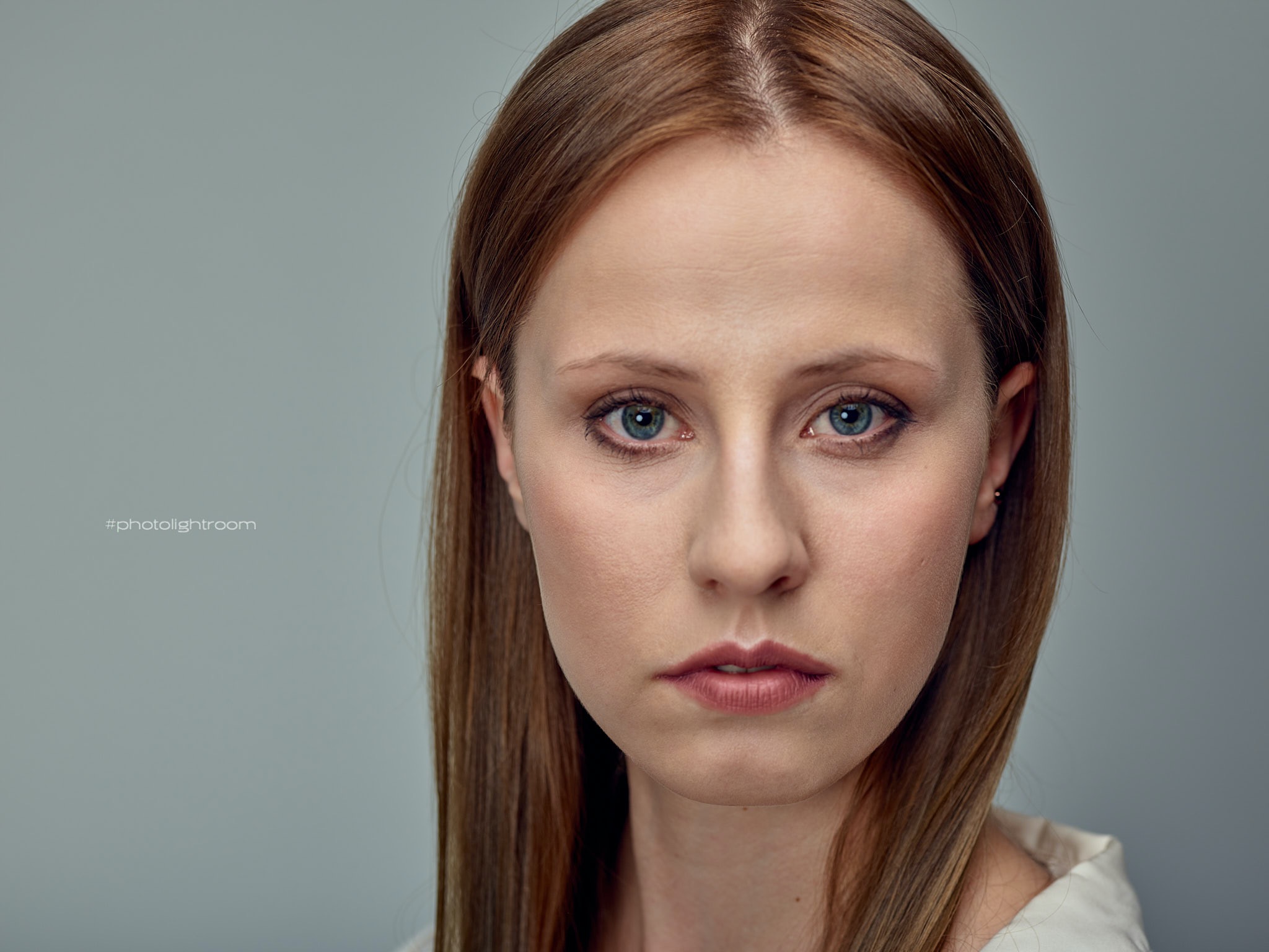 Portret kobiety o jasnej karnacji i niebieskich oczach, z długimi, prostymi, brązowymi włosami na szarym tle.