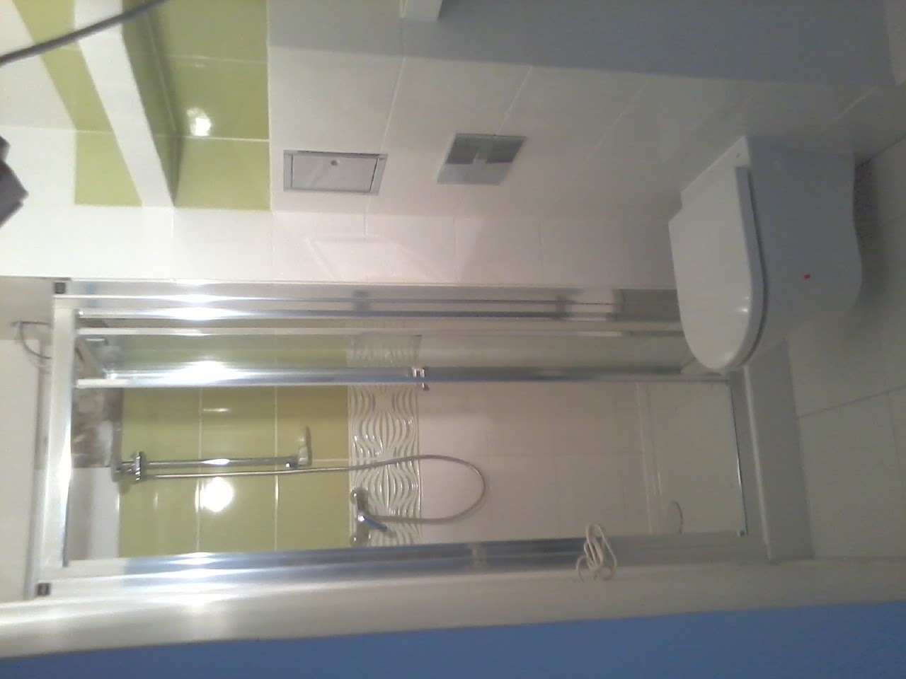 Wykończona łazienka z kabiną prysznicową z przesuwnymi drzwiami, białą toaletą podwieszaną i zielono-białymi płytkami na ścianach.