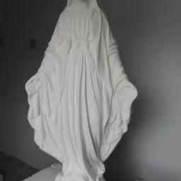 Biała, gipsowa statua Matki Boskiej z rozłożonymi rękami, ustawiona na niskim postumencie, na tle szarej ściany. Widoczny znak wodny w prawym dolnym rogu.