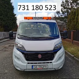 Biały Fiat Ducato z napisem 'Pomoc Drogowa' i numerem telefonu na szybie, zaparkowany na ulicy.