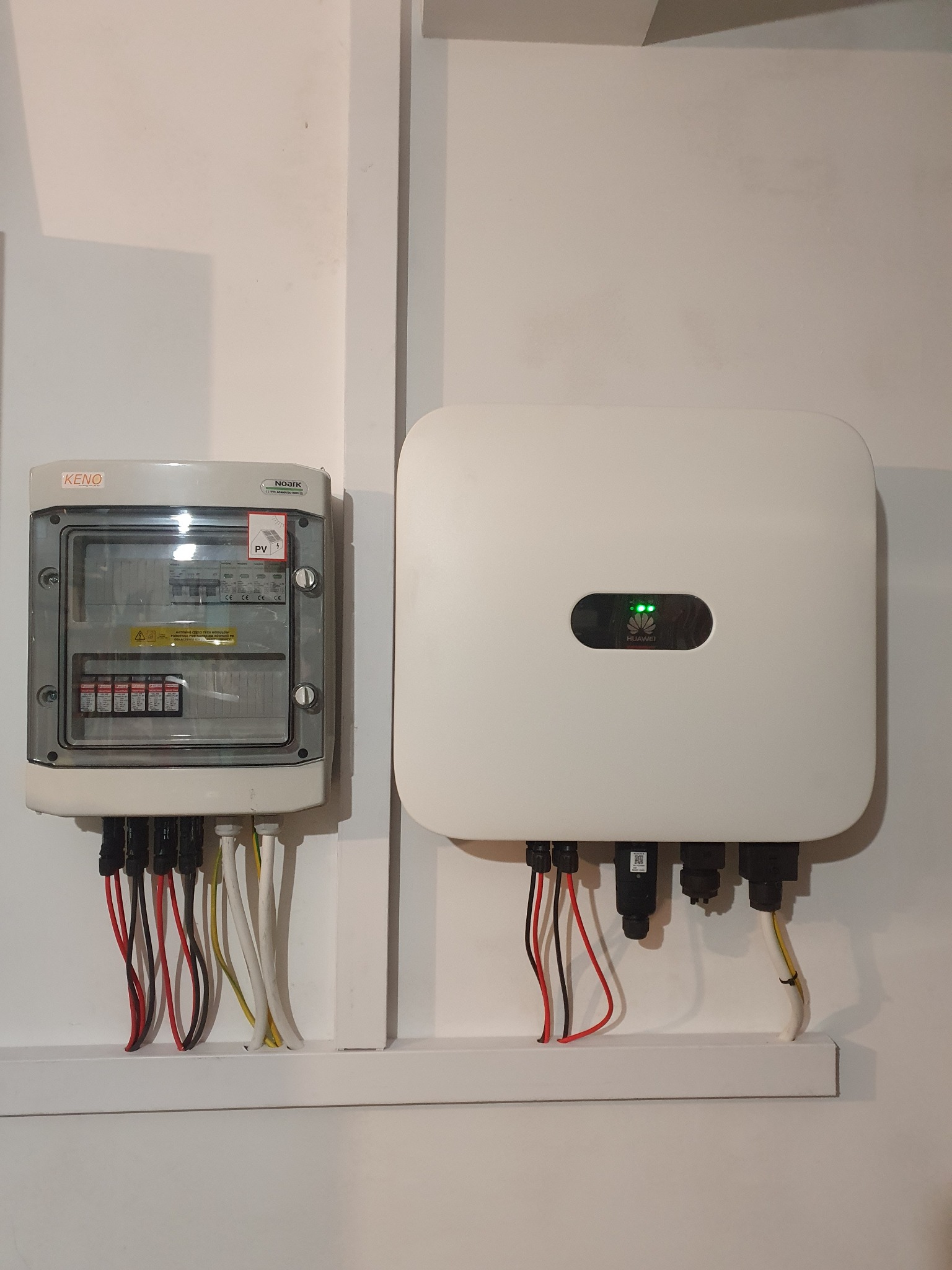 Szczegółowe ujęcie skrzynki bezpiecznikowej i falownika Huawei, elementu instalacji fotowoltaicznej, z widocznymi przewodami i oznaczeniami.