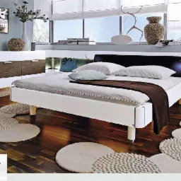 Nowoczesna sypialnia z drewnianą podłogą w odcieniach brązu, białym łóżkiem i szafkami nocnymi z podświetleniem LED, okrągłe dywaniki na podłodze, logo firmy DAWI w rogu.