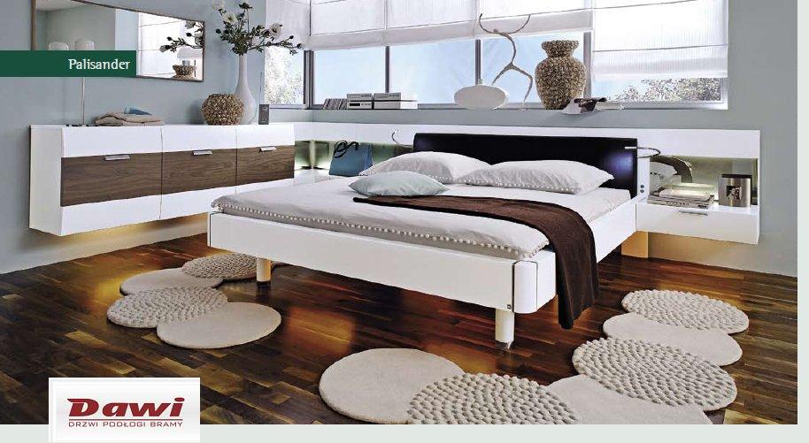Nowoczesna sypialnia z drewnianą podłogą w odcieniach brązu, białym łóżkiem i szafkami nocnymi z podświetleniem LED, okrągłe dywaniki na podłodze, logo firmy DAWI w rogu.