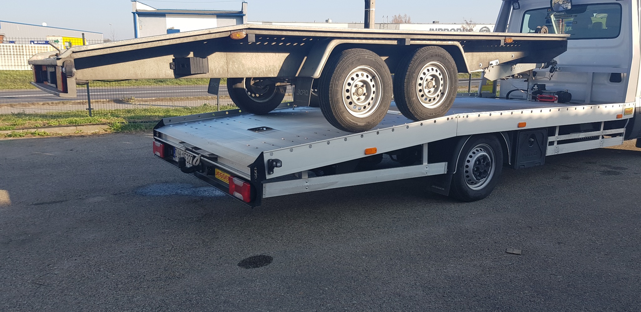 Laweta z najazdem, na której stoi przyczepa z dwoma kołami, widok z tyłu, oświetlenie dzienne.