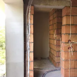 Wewnętrzne ściany z cegły dziurawki z poprowadzonymi przewodami elektrycznymi w peszlach, zabezpieczonymi metalowymi obejmami, widoczne puszki elektryczne z wypuszczonymi przewodami, surowy stan...