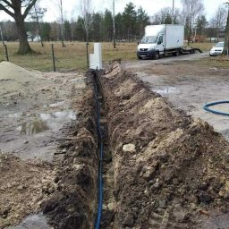 Sun protection system - Wykonany wykop w ziemi z ułożonym niebieskim kablem w karbowanej osłonie, widoczne białe pustaki i samochód dostawczy w tle.