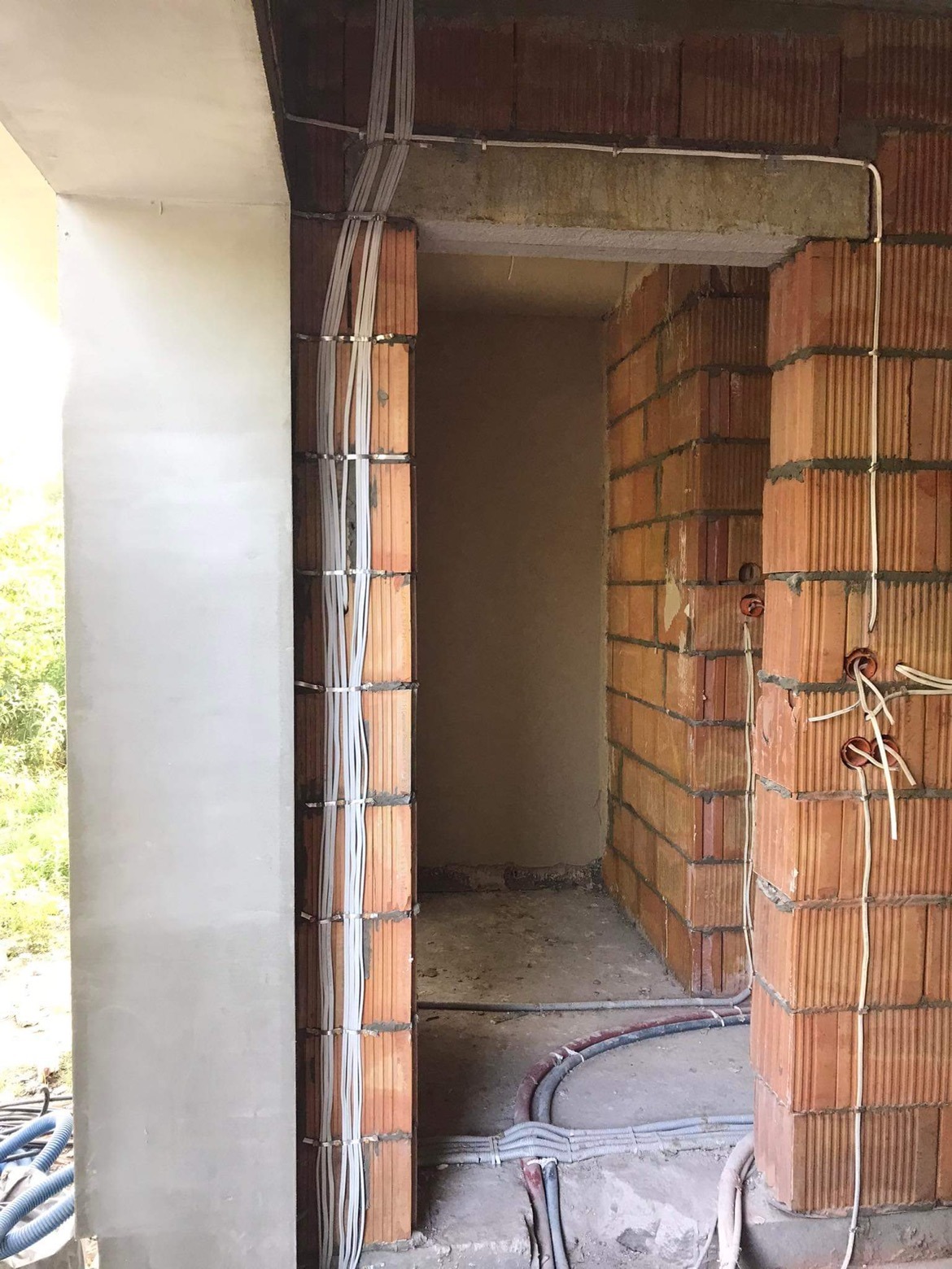 Wewnętrzne ściany z cegły dziurawki z poprowadzonymi przewodami elektrycznymi w peszlach, zabezpieczonymi metalowymi obejmami, widoczne puszki elektryczne z wypuszczonymi przewodami, surowy stan...