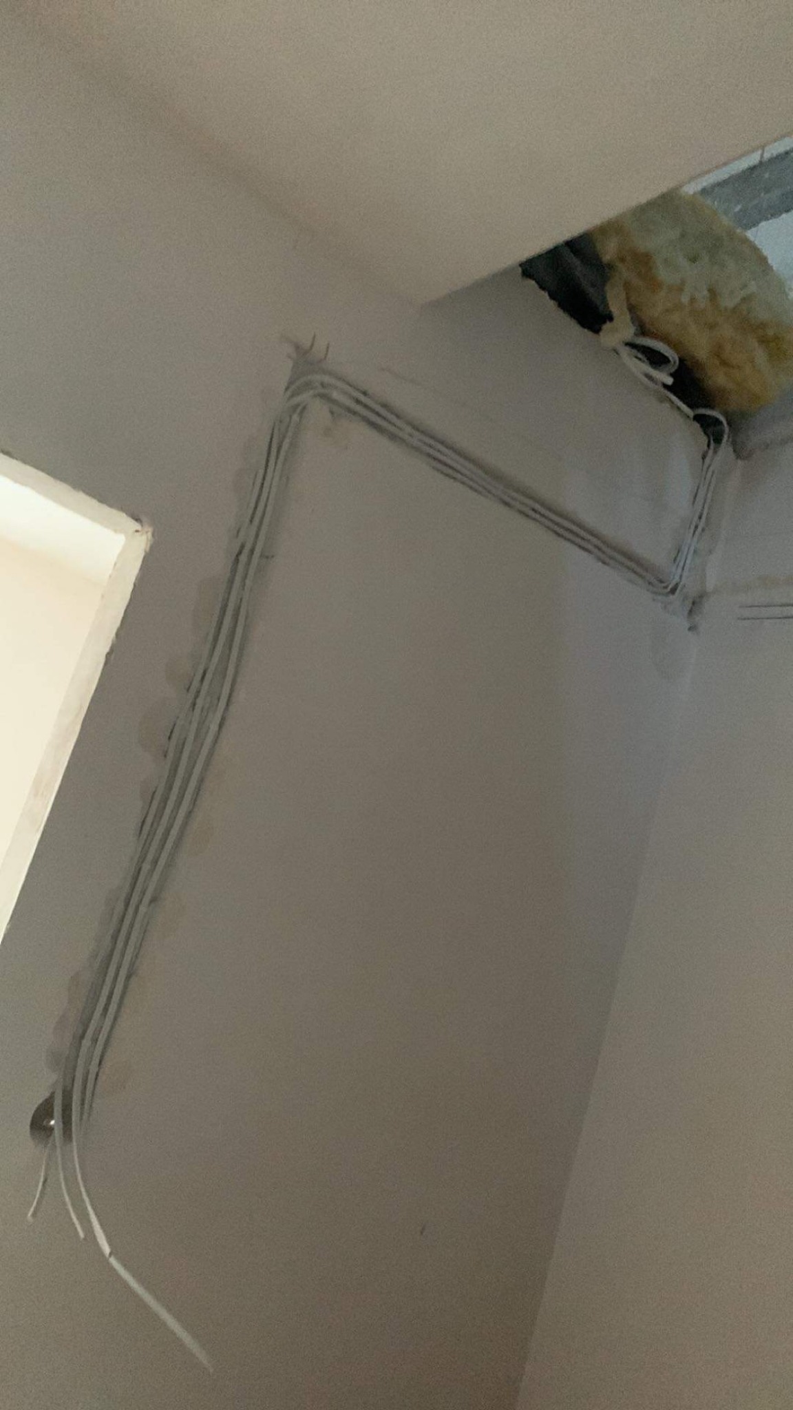 Kable elektryczne prowadzone po ścianie pod sufitem, widoczne otwory w ścianie i izolacja w otworze sufitowym.