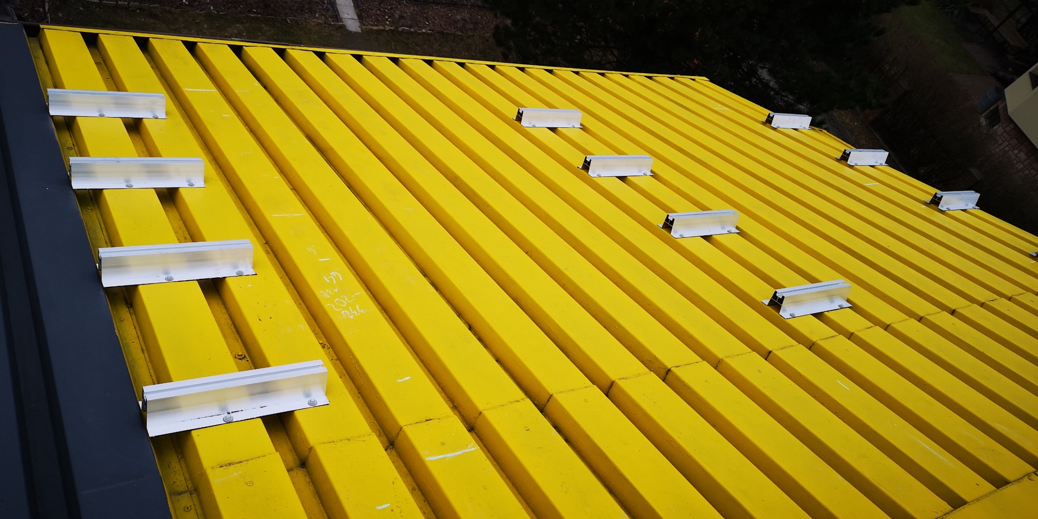 Żółty dach z blachy trapezowej z zamontowanymi aluminiowymi uchwytami do paneli słonecznych, widok z góry pod kątem.