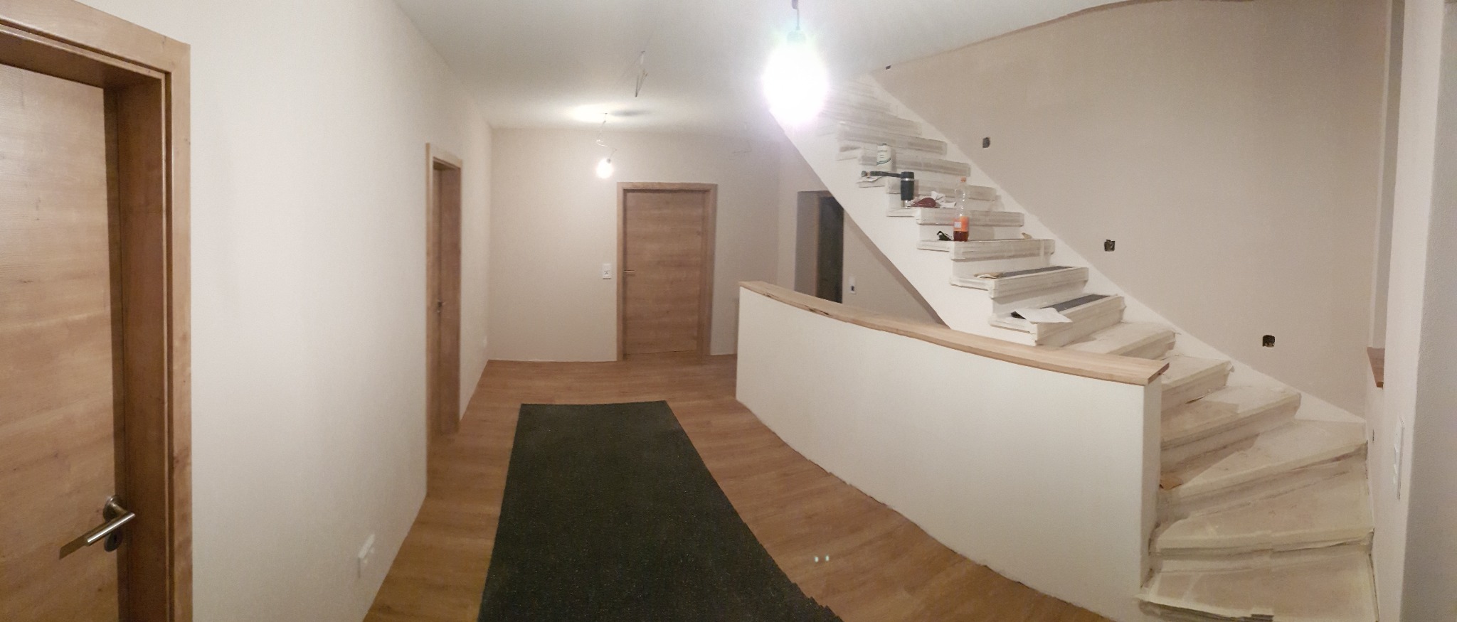 Korytarz w trakcie prac wykończeniowych: ściany przygotowane pod malowanie, schody w trakcie obkładania, widoczne narzędzia i materiały budowlane.