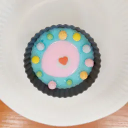 Niebieski deser w foremce na białym talerzu, udekorowany kolorowymi kuleczkami i różowym środkiem z czerwonym serduszkiem.