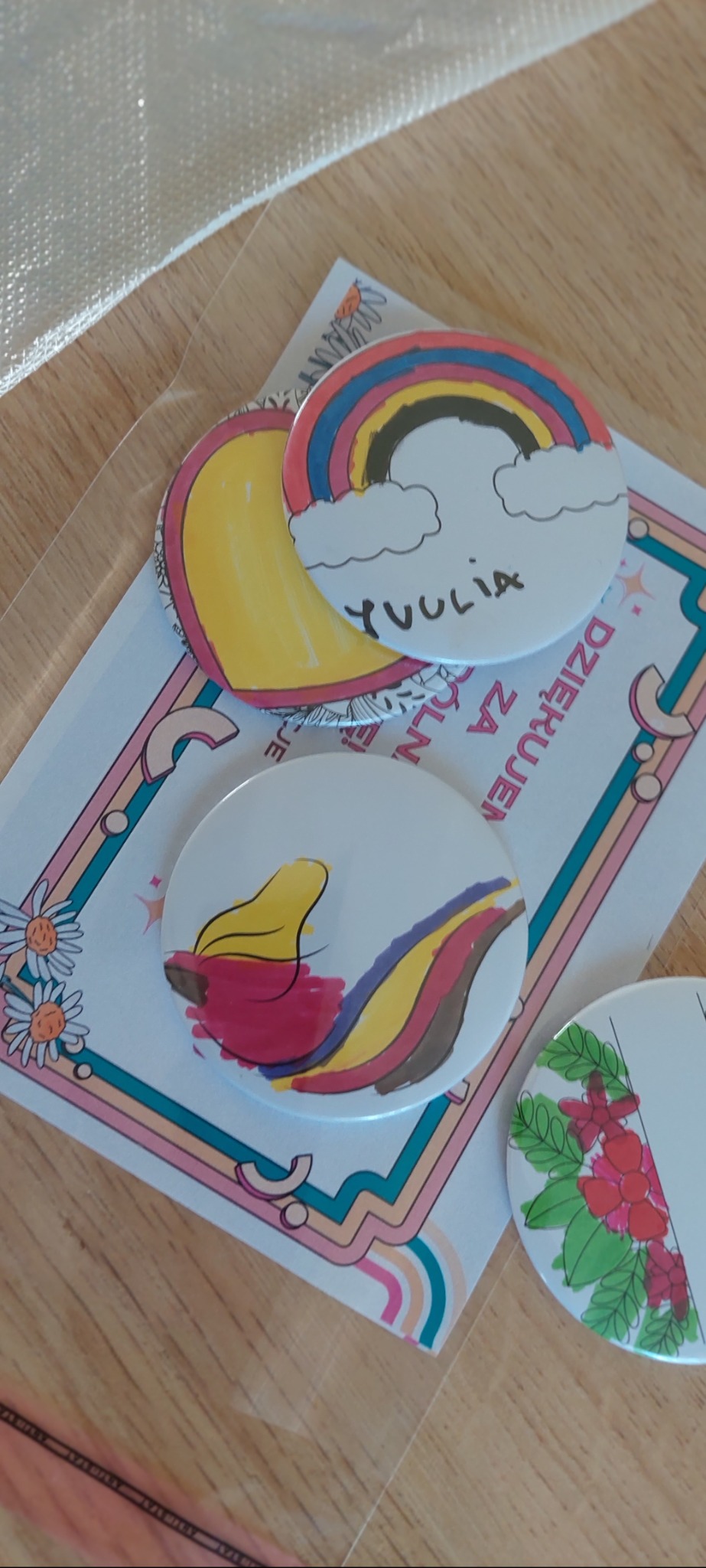 Ręcznie malowane przypinki z motywami tęczy, chmur i kwiatów, umieszczone na kartce z napisem 'Dziękuję za zamówienie'.