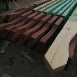 Przygotowane elementy drewniane, niektóre pomalowane na zielono, inne bejcowane na brązowo, leżące na ziemi, prawdopodobnie do budowy altany.