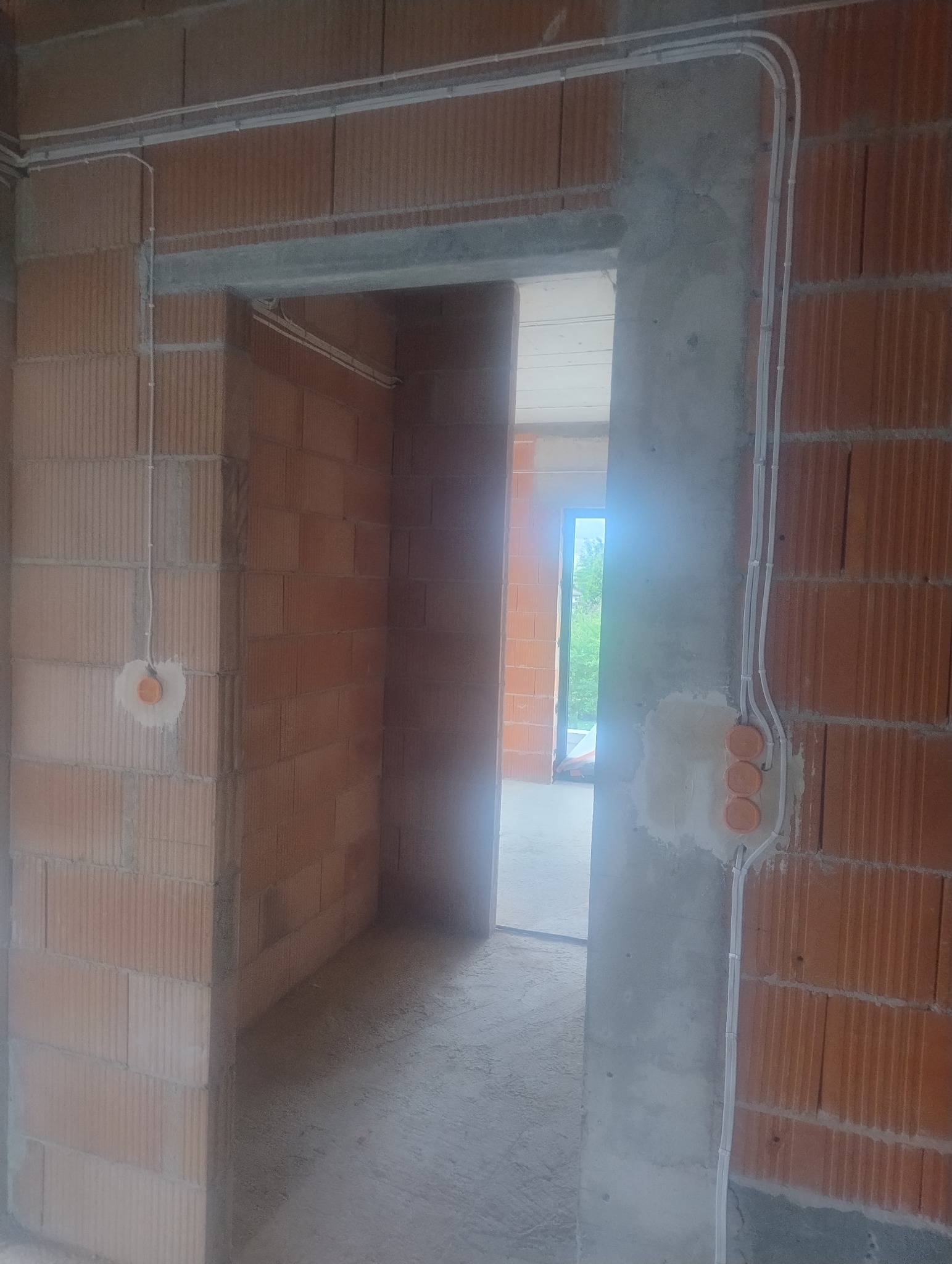 Instalacja elektryczna w surowym wnętrzu: kable w listwach prowadzone po ceglanych ścianach, widoczne puszki pod gniazdka. Etap prac przed wykończeniem.