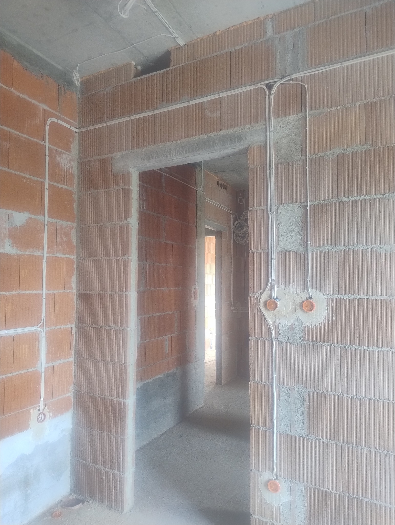 Wnętrze w trakcie prac elektrycznych: kable prowadzone po ścianach z cegły, puszki elektryczne w przygotowanych otworach, surowy betonowy sufit. Instalacja w trakcie realizacji.