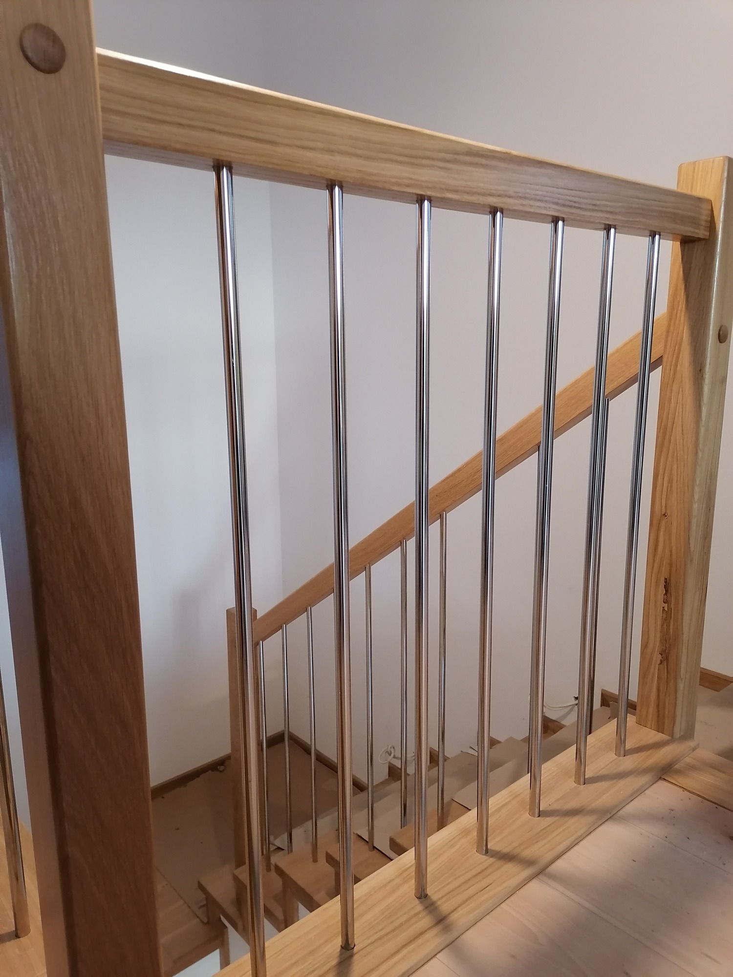 Jasne drewniane schody z metalowymi, pionowymi balustradami, widok z góry na pierwszy bieg, minimalistyczny design.