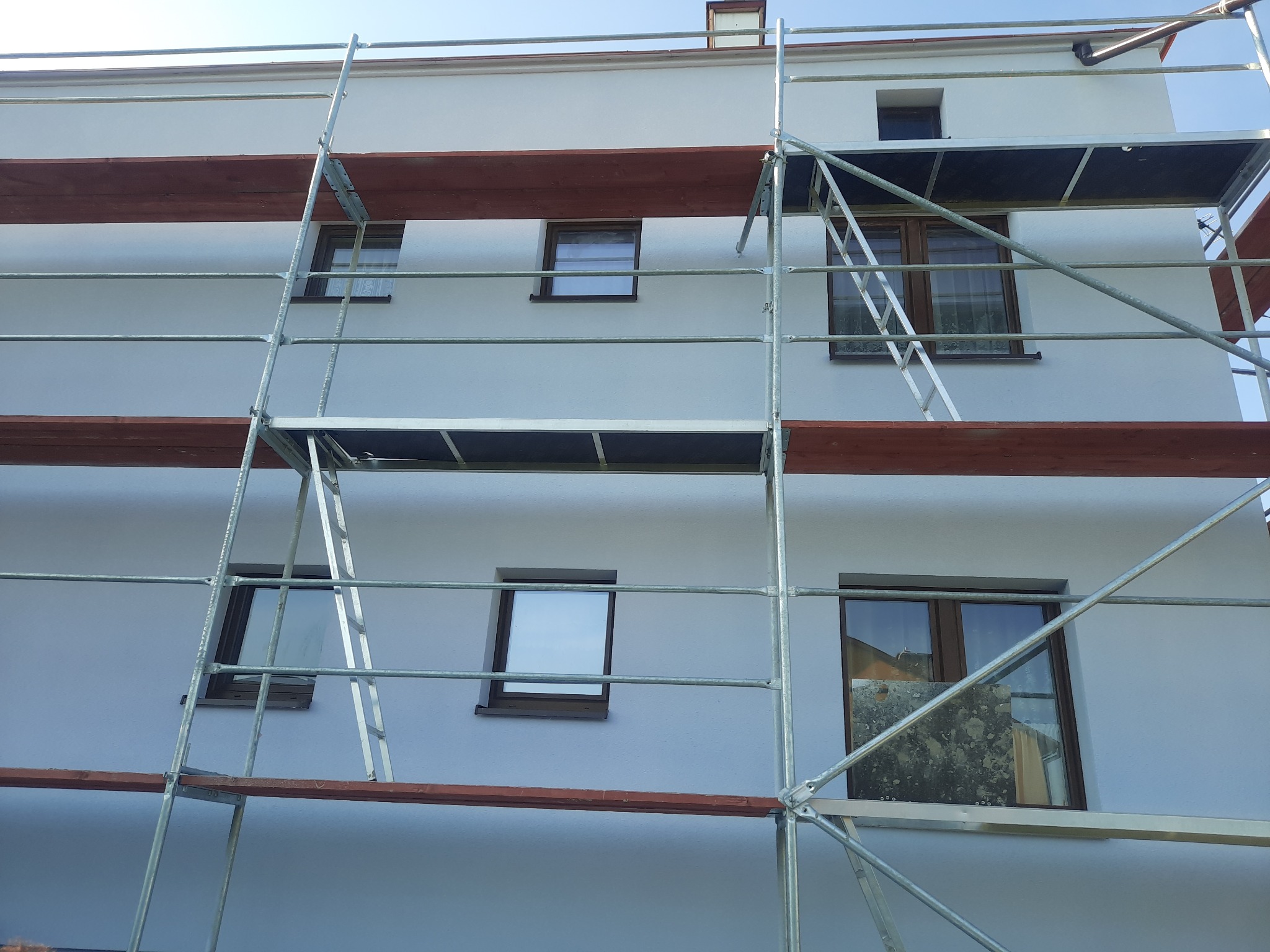 Świeżo otynkowana, biała fasada domu jednorodzinnego z zamontowanym rusztowaniem i widocznymi oknami, przygotowana do dalszych prac wykończeniowych.