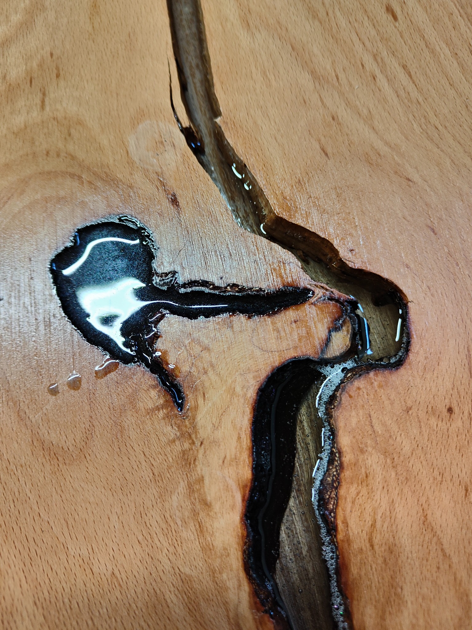 Fragment drewnianego blatu z żywicą epoksydową wypełniającą pęknięcia i ubytki, tworząc unikalny wzór.