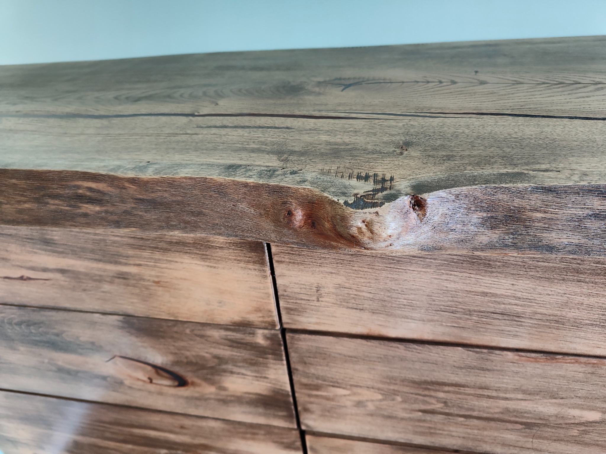 Fragment szafki z blatem z naturalnego drewna o wyraźnym usłojeniu i widocznymi sękami, wykończonego w odcieniach brązu i szarości.