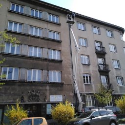 INEL-TEL Grzegorz Libera - Prace na wysokościach przy budynku mieszkalnym z użyciem podnośnika koszowego. Widoczne okna, elewacja i zaparkowane samochody. Dzień słoneczny.