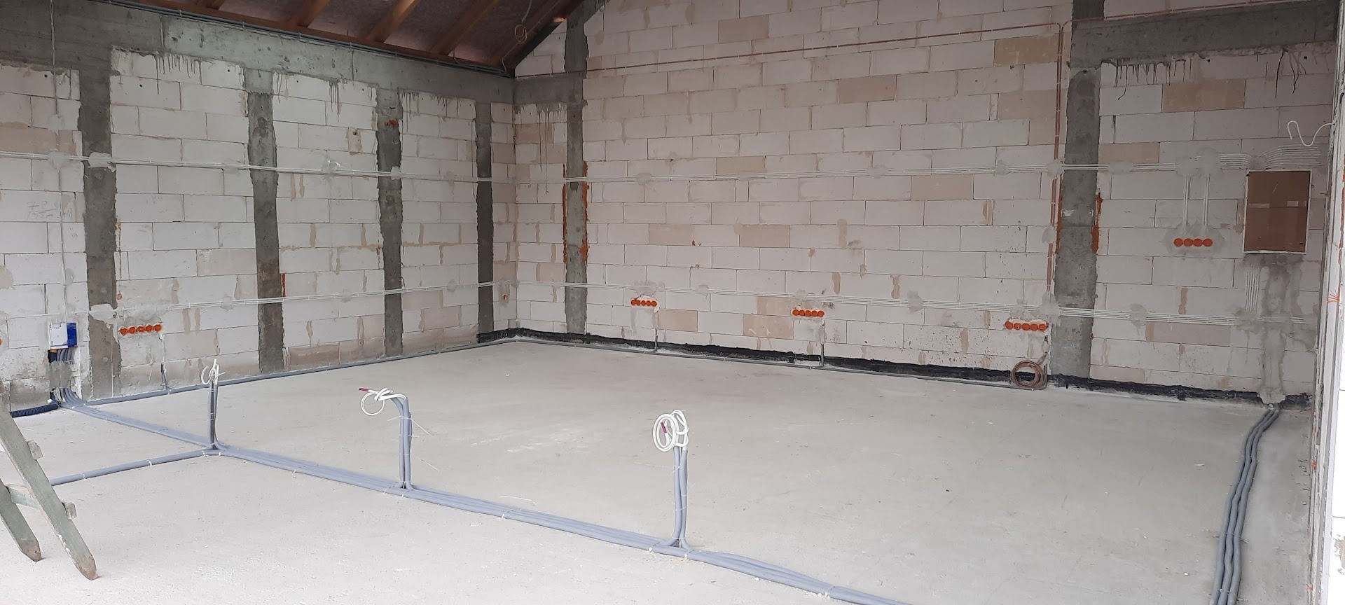 Surowy stan: Instalacja elektryczna w budynku z białego pustaka. Widoczne kable, puszki elektryczne i rury na ścianach i podłodze. Etap prac przed tynkowaniem.