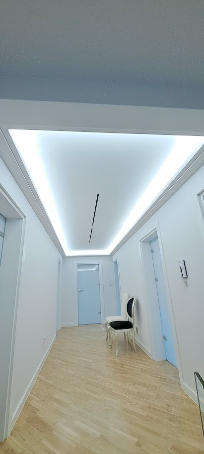 Nowoczesny korytarz z białymi ścianami i podświetlanym sufitem. Dwa krzesła w stylu glamour dodają elegancji. Minimalistyczny design z drewnianą podłogą.